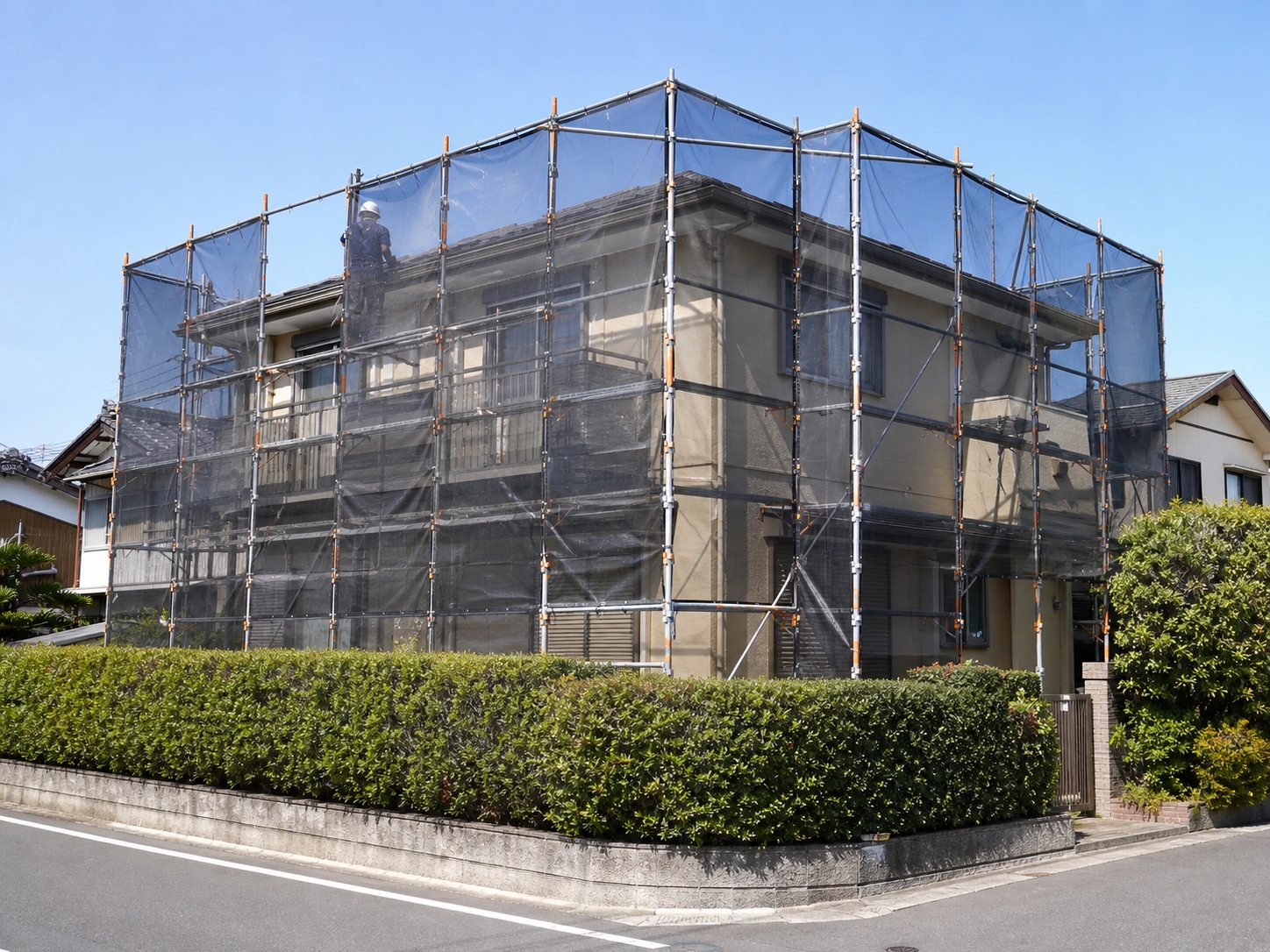 足場とメッシュシートで囲まれた2階建て住宅